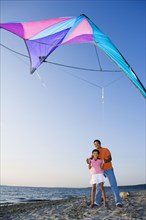 Hispanic father and daughter flying kite at beach
