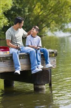 Hispanic father and son fishing on dock