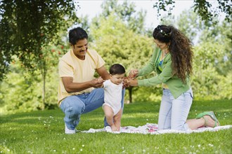 Hispanic parents helping baby walk in park