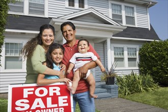 Hispanic family with For Sale sign in front of house