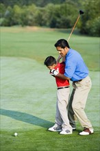 Hispanic father helping son play golf