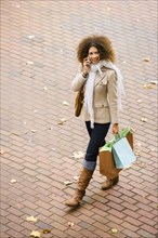 Hispanic woman walking with cell phone and shopping bags