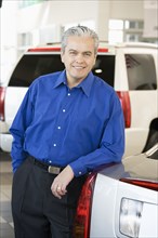 Hispanic car salesman leaning on new car
