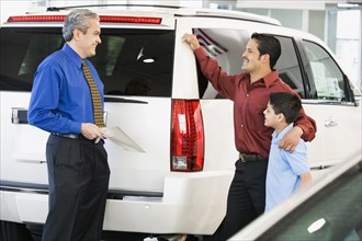 Hispanic car salesman talking to father and son