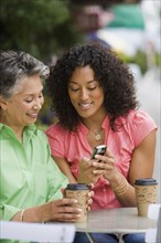 African American mother and adult daughter looking at cell phone