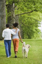 African American mother and adult daughter walking dog