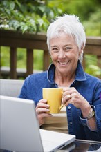 Senior woman with coffee and laptop outdoors