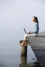 Asian woman holding laptop on edge of pier