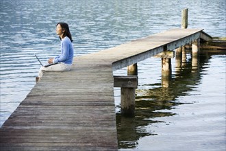 Asian woman holding laptop on edge of pier