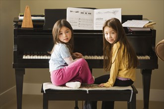 Asian sisters sitting at piano