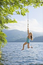 Asian girl hanging from lake rope swing