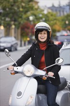 Mixed race woman in helmet driving scooter