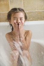 Mixed race young girl being sprayed with water in bathtub