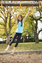 Mixed race young girl swinging from playground equipment