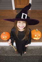 Mixed race young girl in witch costume with Halloween pumpkins