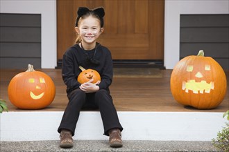 Mixed race young girl in cat costume holding Halloween pumpkin