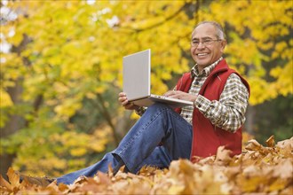 Hispanic man using laptop sitting in autumn leaves