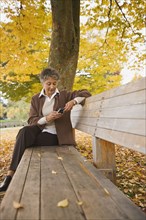 African woman using cell phone on park bench in autumn