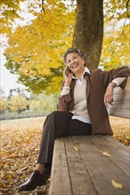 African woman talking on cell phone on park bench in autumn