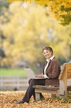 African woman using laptop on park bench in autumn