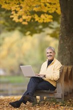 African man using laptop on park bench in autumn