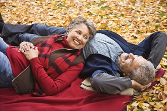 African couple laying on blanket among autumn leaves
