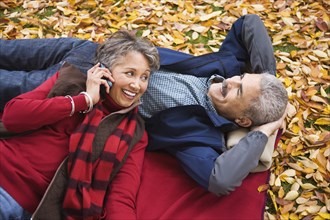 African couple laying on blanket in autumn with cell phone