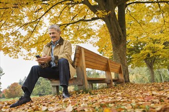 African man using cell phone on park bench in autumn