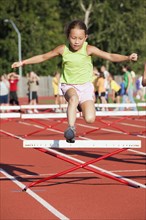 Mixed race girl jumping over hurdle