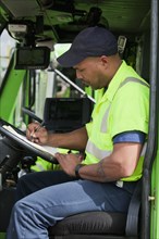 African American man in garbage truck writing on clipboard