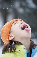 Mixed race girl catching snowflakes on tongue