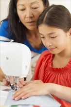 Mother teaching girl to use sewing machine
