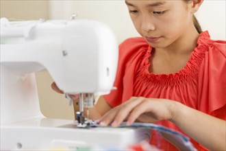 Mixed race girl using sewing machine