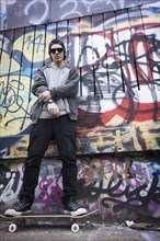 Caucasian teenage boy on skateboard by graffiti wall