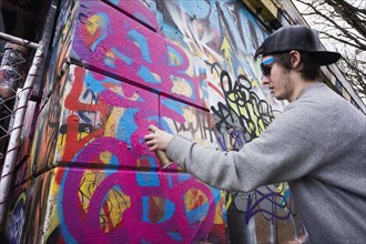 Caucasian boy spraying graffiti on urban wall