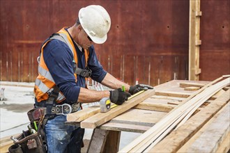 Caucasian worker measuring wood at construction site