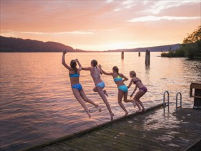 Girls jumping into lake from wooden dock