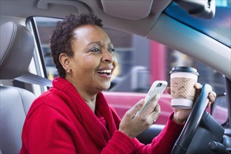Black woman using cell phone and drinking coffee while driving car