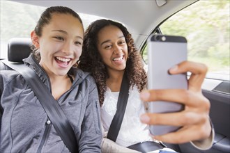 Teenage girls using cell phone in car back seat