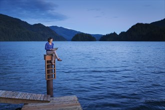 Japanese woman sitting on wooden dock at lake