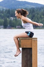 Mixed race girl sitting on wooden pedestal at lake