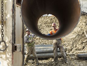 Caucasian workers hauling pipe at construction site