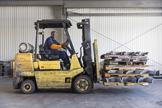 Black worker driving forklift in factory