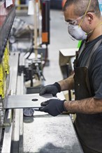Hispanic worker wearing mask fabricating metal in factory
