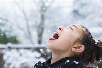 Mixed Race girl catching snowflakes on tongue