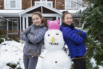 Mixed Race girls posing with snowman wearing pink hat with ears