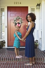 Smiling mixed race mother and daughter standing on front stoop