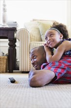 Mixed race father and daughter laying on floor watching television