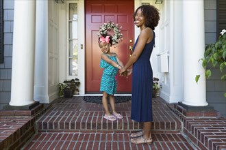 Portrait of smiling mixed race mother and daughter on front stoop