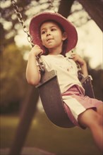 Mixed race girl playing on swing on playground
